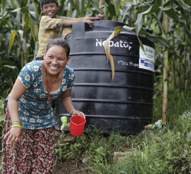 Woman and her son in Nepal getting fresh water from a black plastic drum