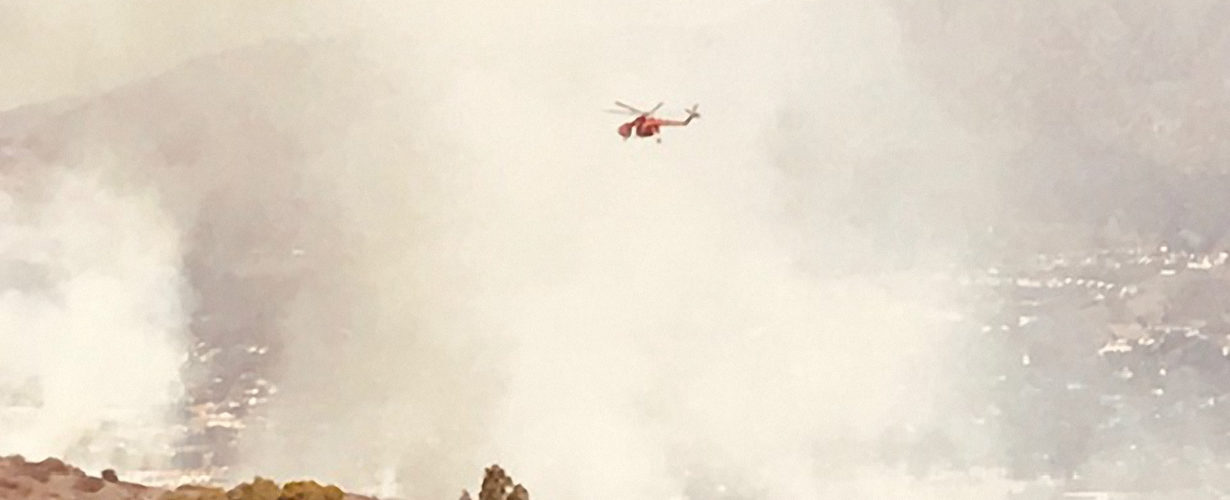 Helicopter flies over burning mountain hillside